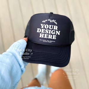 May include: A black trucker hat with a white mesh back. The hat has the text "Mock City Studio" and "YOUR DESIGN HERE" in white lettering.