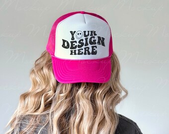Op de afbeelding: Een roze en witte truckercap met een zwart mesh achterpaneel. De voorkant van de cap heeft een wit paneel met de tekst "YOUR DESIGN HERE" in zwart.