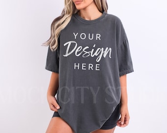Puede incluir: Una camiseta gris oscuro de gran tamaño con el texto "YOUR Design HERE" impreso en blanco en la parte delantera.