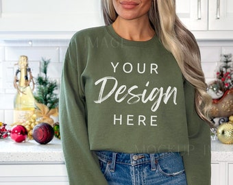 May include: A woman wearing a green sweatshirt with the text "YOUR Design HERE" on the front. She is standing in a kitchen with a white countertop and cabinets.