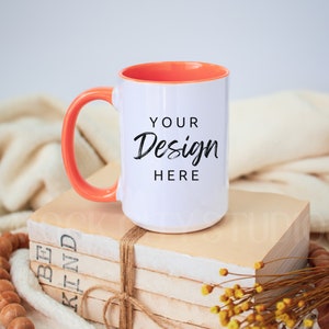 May include: White ceramic mug with an orange rim and handle. The mug is sitting on a stack of books with a brown twine bow. The mug has the text "YOUR Design HERE" printed on it.