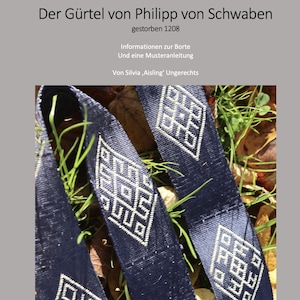 Puede incluir: Dos cinturones de tela azul con patrones geométricos blancos tejidos en la tela. Los cinturones están sobre una cama de hierba verde.