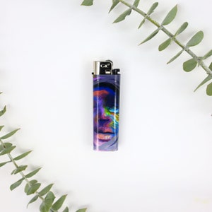May include: A colorful lighter with a blue, purple, and pink abstract design. The lighter is a standard size and has a silver top with the word "Clipper" printed on it.