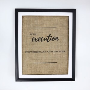 May include: A framed burlap print with the word "execution" in black cursive lettering. The print also includes the text "NOUN" and "STOP TALKING AND PUT IN THE WORK".