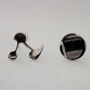 May include: A pair of silver earrings. One is a simple disc, the other has a distinctive design with two spheres linked by a curved line and a pointed shape. The earrings are shown on a white surface.
