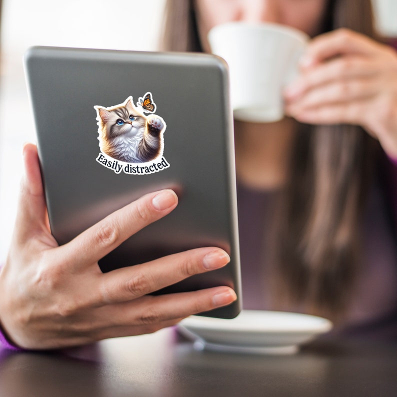 May include: A gray tablet computer with a sticker of a cat with a butterfly on its paw. The sticker says "Easily distracted".