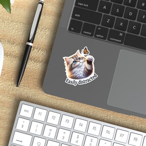 May include: A sticker featuring a cartoon cat with blue eyes looking up at a butterfly. The text "Easily distracted" is below the cat.