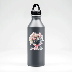 May include: A gray reusable water bottle with a black lid and handle. A sticker of a pink and white flower bouquet is on the bottle.