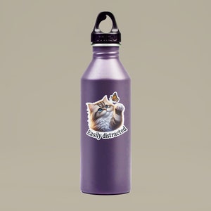 May include: A purple stainless steel water bottle with a black lid and a sticker of a cat looking at a butterfly with the text "Easily distracted".