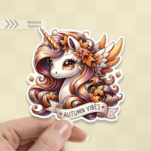 K&ouml;nnte beinhalten: Ein Aufkleber mit einem Cartoon-Einhorn mit goldenem Horn und herbstlichem Haar und Fl&uuml;geln. Das Einhorn hat ein wei&szlig;es Gesicht, gro&szlig;e Augen und ist mit Herbstbl&auml;ttern und -bl&uuml;ten geschm&uuml;ckt. Ein Banner darunter lautet "AUTUMN VIBES".