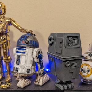 May include: A collection of four Star Wars action figures, including a gold C-3PO, a white and blue R2-D2, a gray Imperial droid, and a brown and yellow BB-8.