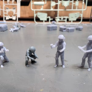 Puede incluir: Cinco figuritas de plástico gris de personas que llevan cascos. Las figuritas están en diferentes posiciones, algunas sosteniendo herramientas.