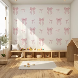 Op de afbeelding: Een lichte kamer met een houten vloer en ingebouwde planken. De muur is versierd met een herhalend patroon van roze strikken. De kamer bevat houten speelgoed, een wit tapijt en een geweven mand met een plant.