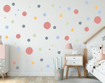 May include: A white wall with colorful polka dot wall decals in shades of pink, blue, green, and yellow. The decals are scattered randomly across the wall. There is a bed with a white headboard and a pink flamingo toy in the corner of the room.