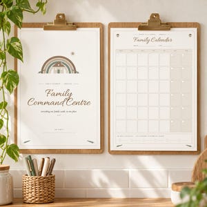 May include: Two wooden clipboards holding printed paper sheets. The left sheet features a rainbow graphic, a house icon, and the text Family Command Centre. The right sheet displays a monthly Family Calendar grid with blank boxes.