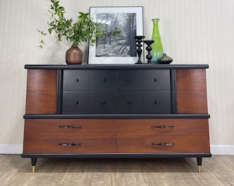 May include: A mid-century modern dresser with six drawers, featuring a black painted finish and wood veneer accents. The dresser has brass legs and black drawer pulls.