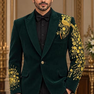 May include: A dark green velvet blazer featuring intricate gold embroidery on the left shoulder and sleeve, depicting a peacock and floral motifs. The blazer has a single button closure, notched lapels, and is worn over a black shirt and bow tie.