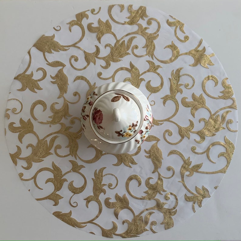 May include: White round tablecloth with a gold floral pattern. A white porcelain sugar bowl with a floral design sits in the center of the tablecloth.
