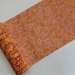 May include: A roll of pink and orange tulle with a gold glitter pattern. The tulle has a floral design and is ideal for decorating a party or wedding.
