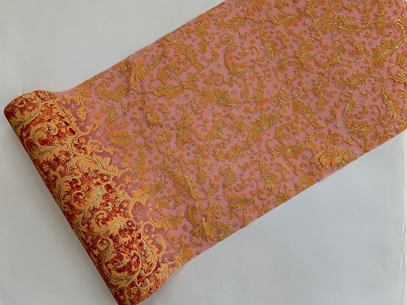 May include: A roll of pink and orange tulle with a gold glitter pattern. The tulle has a floral design and is ideal for decorating a party or wedding.