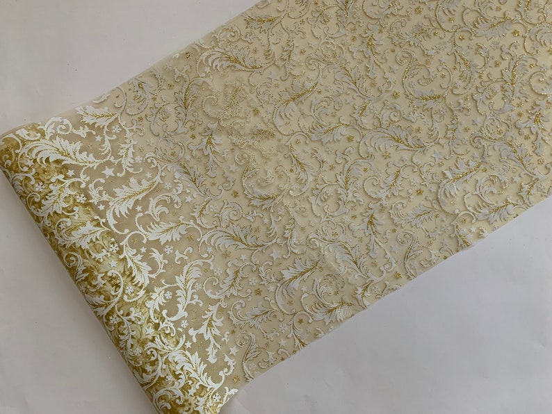 May include: A gold and white table runner with a delicate floral pattern. The runner is made of a sheer fabric with a subtle shimmer.