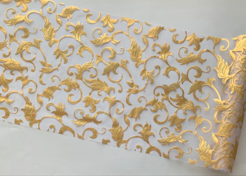 May include: White sheer fabric with a gold metallic pattern of swirling vines and leaves. The fabric is translucent and has a delicate, elegant look.