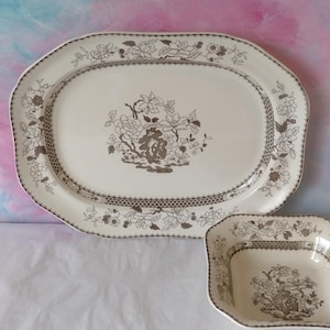 May include: Cream-coloured oval serving platter and a smaller square dish with a brown floral pattern. The edges of both pieces are decorated with a delicate floral and geometric border. The centre of each piece features a detailed floral design.