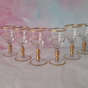 May include: A set of six clear wine glasses with gold rims and gold spiral detailing. The stems and bases are gold-trimmed. The glasses are displayed on a white surface. Each glass is approximately 15 cm tall.