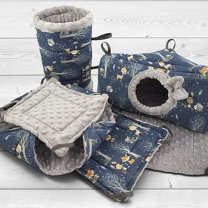 May include: A set of small animal bedding accessories in navy blue fabric with a forest animal print featuring foxes, deer, and trees. The set includes a tunnel, a rectangular hideout with a circular opening, and soft gray dimpled fabric mats.