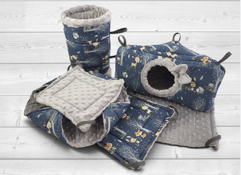 May include: A set of small animal bedding accessories in navy blue fabric with a forest animal print featuring foxes, deer, and trees. The set includes a tunnel, a rectangular hideout with a circular opening, and soft gray dimpled fabric mats.