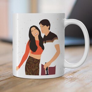 May include: White ceramic mug featuring a couple embracing, with a minimalist illustration style. The woman wears an orange top and patterned skirt, while the man is in a white shirt with brown accents. The mug has a white handle and a light background.