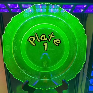 May include: A green glass plate with a decorative etched design. The plate is labelled "Plate 1".