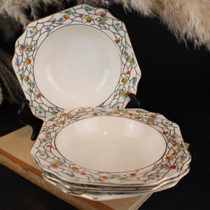 Peut inclure: Un ensemble de bols en céramique blanche avec un bord festonné et une bordure dorée. La large bordure présente un motif craquelé noir rempli de petits motifs floraux peints à la main dans des tons orange, bleu, jaune et vert.