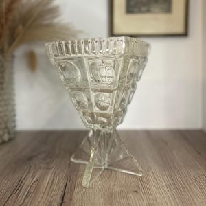 Könnte beinhalten: Eine klare Glasvase mit geometrischem Design und einem dreibeinigen Sockel.