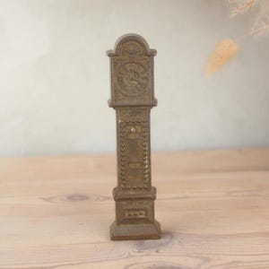 May include: A small, antique-style brass clock. The clock has a rectangular body with a detailed clock face and decorative embellishments. The clock's face shows the time. The clock is a decorative item.