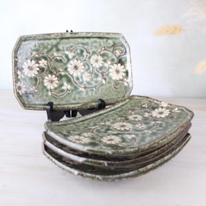May include: A set of four green ceramic rectangular plates with a white floral design. The plates are stacked on top of each other.
