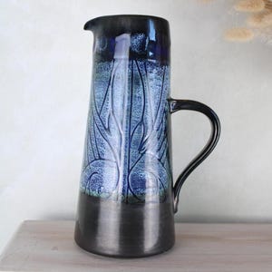 May include: A blue and black ceramic pitcher with a white floral design. The pitcher has a wide base and a narrow neck.
