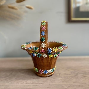 May include: A small brown ceramic basket with a handle decorated with colourful flowers. The basket is ideal for holding small items or trinkets.