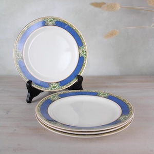 May include: Set of four white ceramic plates with a blue and green floral border. The plates are stacked on top of each other.