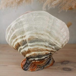 Peut inclure: Sculpture décorative en céramique en forme de champignon. Le design est composé de couches de couleurs allant du blanc au marron et à l'orange. La base est orange foncé et le dessus est blanc.
