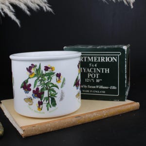 May include: A white ceramic Portmeirion hyacinth pot featuring a botanical illustration of Viola Tricolor flowers and butterflies. The pot is accompanied by its original dark green box, which displays the text Portmeirion 5x4 Hyacinth Pot 12.5cm x 10cm.
