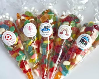 May include: Five clear plastic cone-shaped bags filled with assorted colourful gummy sweets. Each bag is tied with a white ribbon and features a circular sticker with text and graphics, including a football, a fairy, a race car, a rainbow, and a tractor.