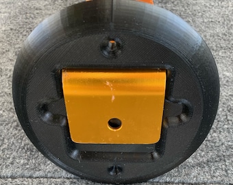 May include: A black circular base with a gold metal bracket attached to it. The bracket has a hole in the center and is secured to the base with four screws.