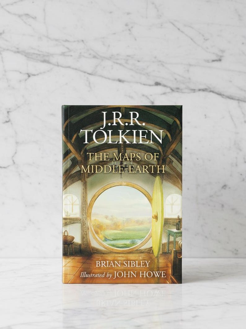 May include: A hardcover book titled "The Maps of Middle-earth" by J.R.R. Tolkien, illustrated by John Howe. The book cover features a detailed illustration of a round doorway with a scenic view, and the author's and illustrator's names.