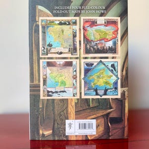 May include: The back cover of a book featuring four full-color fold-out maps by John Howe. The maps are framed and depict various landscapes. The book has a dark green and brown background with the word "TOLKIEN" visible.