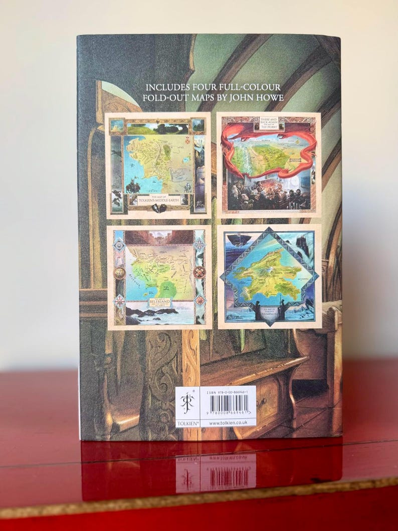 May include: The back cover of a book featuring four full-color fold-out maps by John Howe. The maps are framed and depict various landscapes. The book has a dark green and brown background with the word "TOLKIEN" visible.