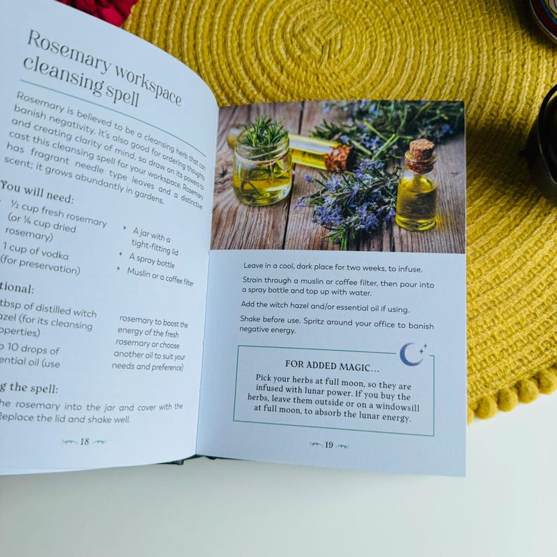 May include: A book with a green cover and white text that reads "Rosemary workspace cleansing spell". The book is open to a page with instructions on how to make a rosemary cleansing spray. The page includes a photo of a glass bottle filled with a yellow liquid and rosemary sprigs. The text also includes a section titled "For Added Magic..." with a crescent moon symbol.