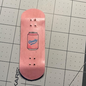 Puede incluir: Fingerboard rosa con un gráfico de una lata de refresco que dice "Cloudy".