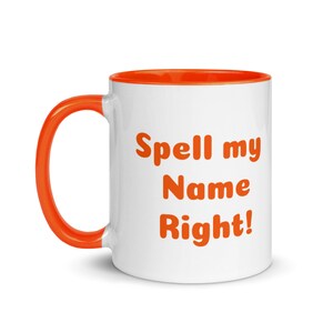 May include: White ceramic mug with an orange interior and handle. The mug features the text "Spell my Name Right!" in orange, bold letters. A simple, yet eye-catching design for coffee or tea.