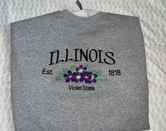 May include: Gray sweatshirt with the text "ILLINOIS Est. 1818 Violet State" and an embroidered purple flower design.